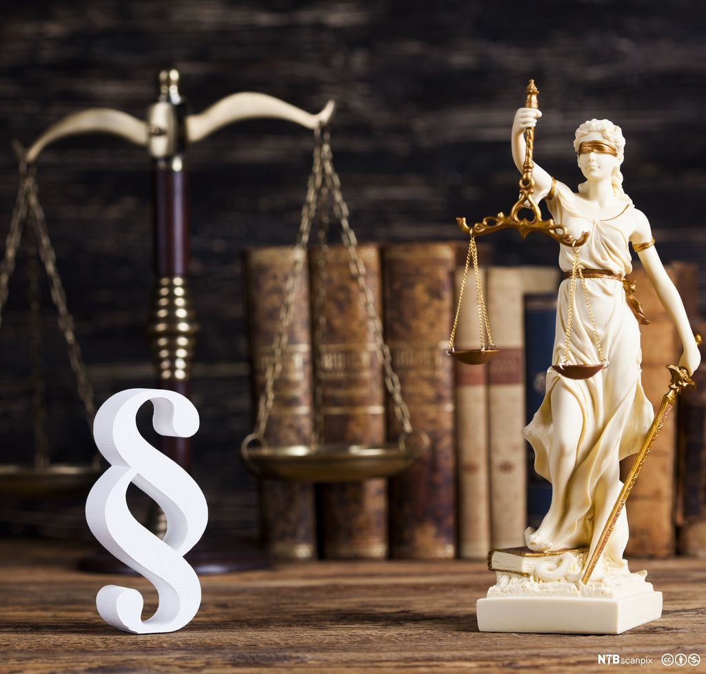 Fru Justitia som held ei vekt. Illustrasjon av ein lovparagraf i forgrunnen. Foto.