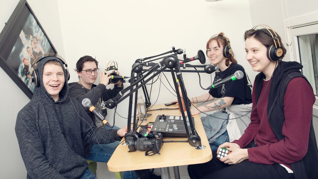 Fire elever, to gutter og to jenter, sitter overfor hverandre i et lydstudio. De har hodetelefoner på og hver sin mikrofon foran seg. Foto.