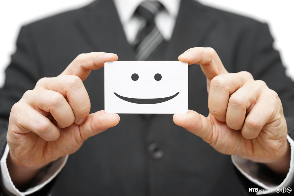 Mann i dress holder et kort med et smileansikt. Foto.