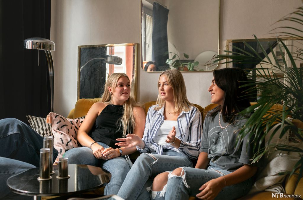 Tre venninner sitter i en sofa og snakker sammen. Foto. 