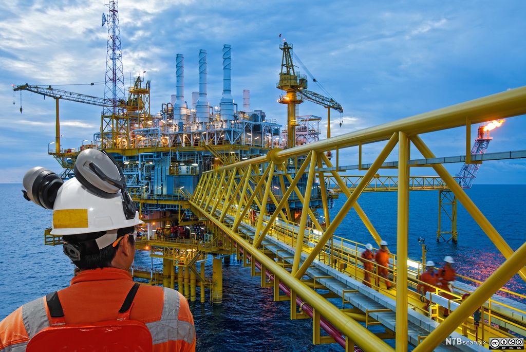 Offshore-arbeider med hjelm, øreklokker og vernebriller ser over til en gangbro mellom to plattformer.  Foto.