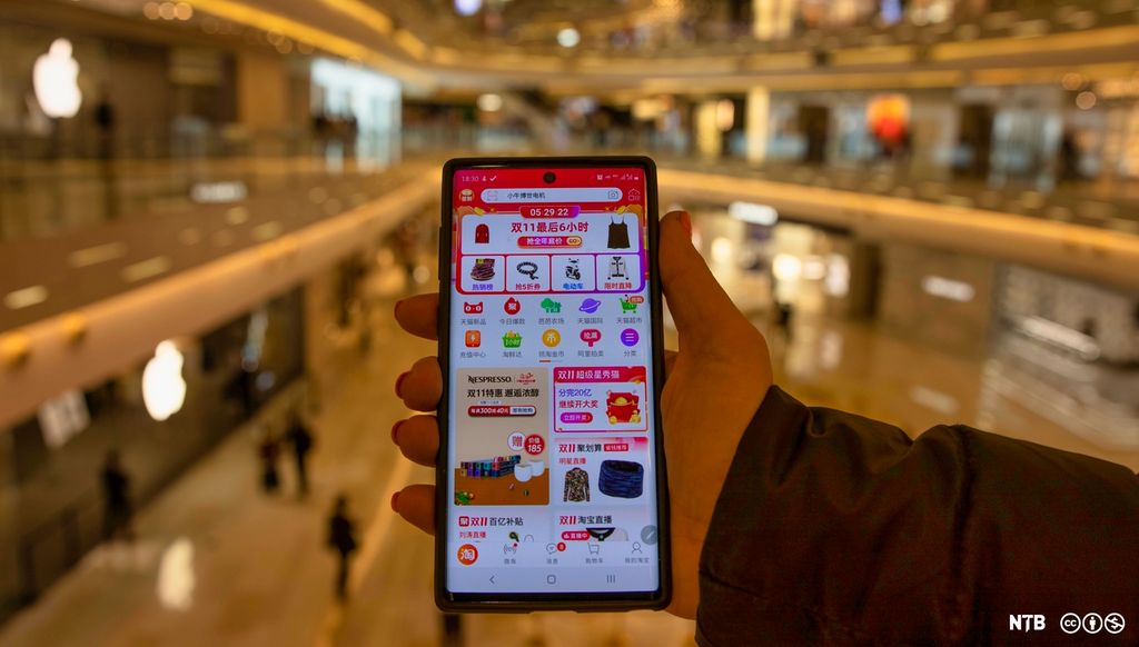 Ei hånd holder en mobil med mange fargerike apper. Skriftspråket er kinesisk. Foto.