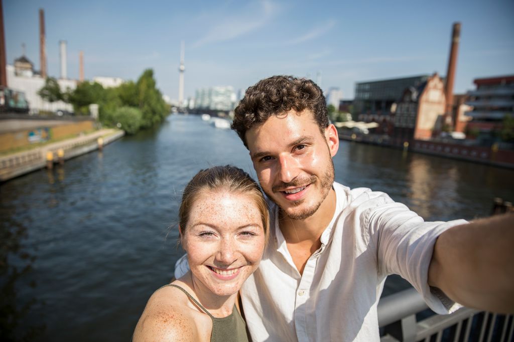 Ungt par tar selfie med vann og by i bakgrunnen. Foto.