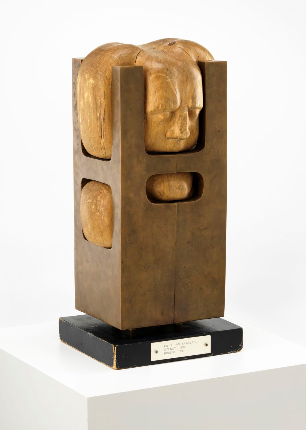 Treskulptur av et hode som er stengt inne i en boks av bronse som er for trang. Foto.