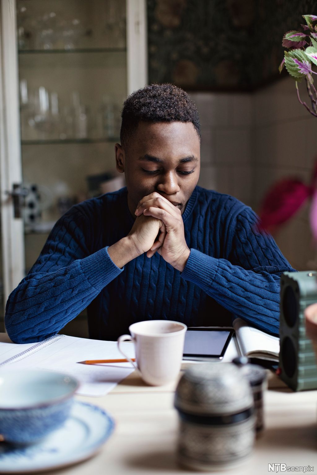 Ung gutt i blå genser sitter med skolearbeid ved et bord. Foto.