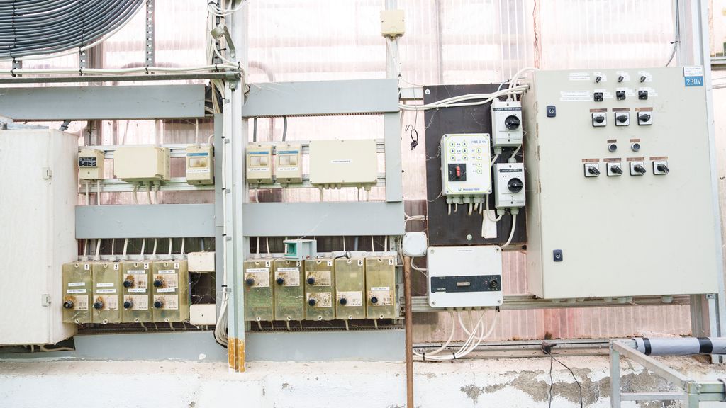 Eltavler på vegg i veksthus med ledninger og brytere. Foto.