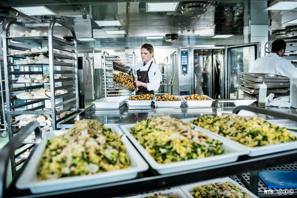 Et storkjøkken der to kokker holder på med å legge opp mat på fat. Foto.