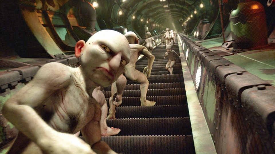 Utsnitt fra filmen "Rulletrappen". Flere nakne mannsfigurer går oppover ei rulletrapp. De er skallete på hodet og har overdimensjonerte ansikstrekk. En av mannsfigurene går motsatt vei i rulletrappa, og en annen ser bakover med et misfornøyd uttrykk i ansiktet. Foto.