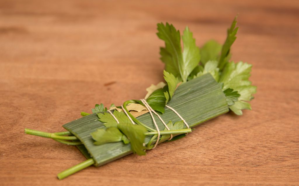 En ferdigbundet krydderkvast med persille, purreløk og laubærblader liggende på ei skjærefjøl. Foto.