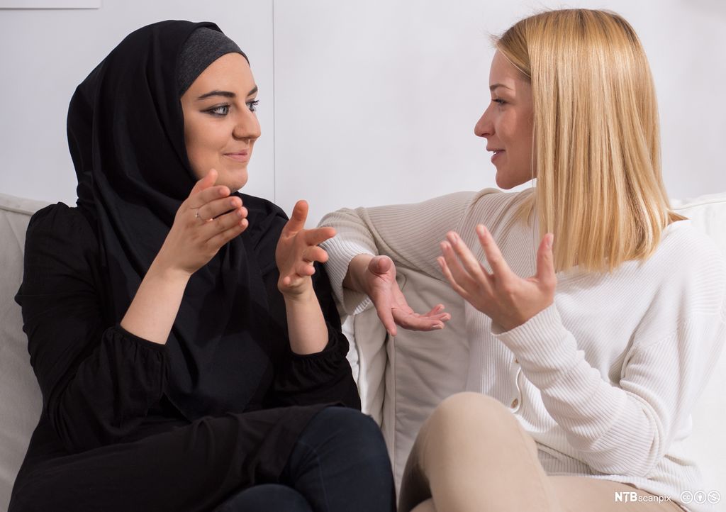 Jente med hijab samtaler med blond langhåret jente. Foto.