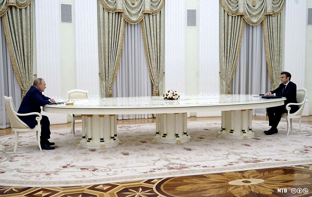 Foto av to menn i mørk dress som sitter ved hver sin ende av et kjempelangt hvitt bord i et presidentpalass.