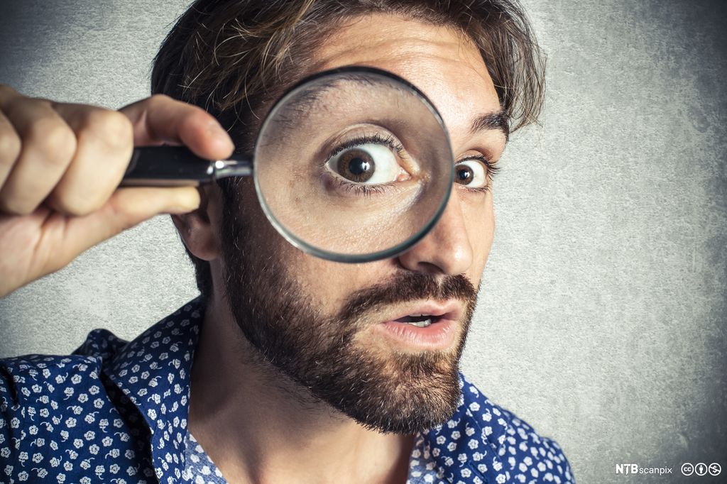Mann som ser gjennom et forstørrelsesglass. Foto. 