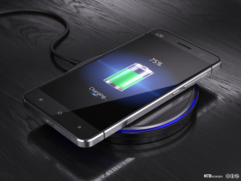 Mobiltelefon ligger på trådløs lader. Foto.