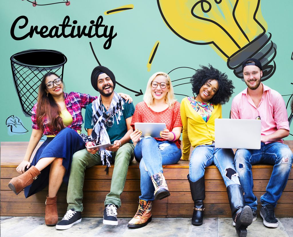 En rekke studenter i fargerike klær sitter på en benk og smiler foran en tavle med en stor, lysende lyspære med ressursikoner rundt. Foto.