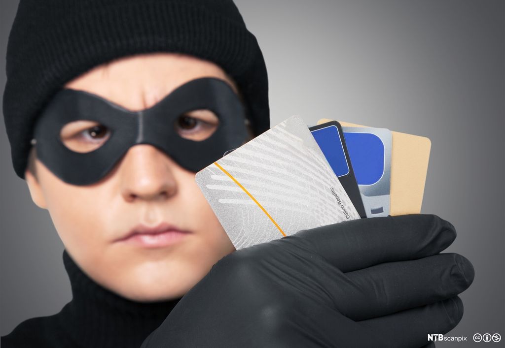 Mann bruker maske for å skjule identiteten. Han viser fram fire bankkort. Foto.