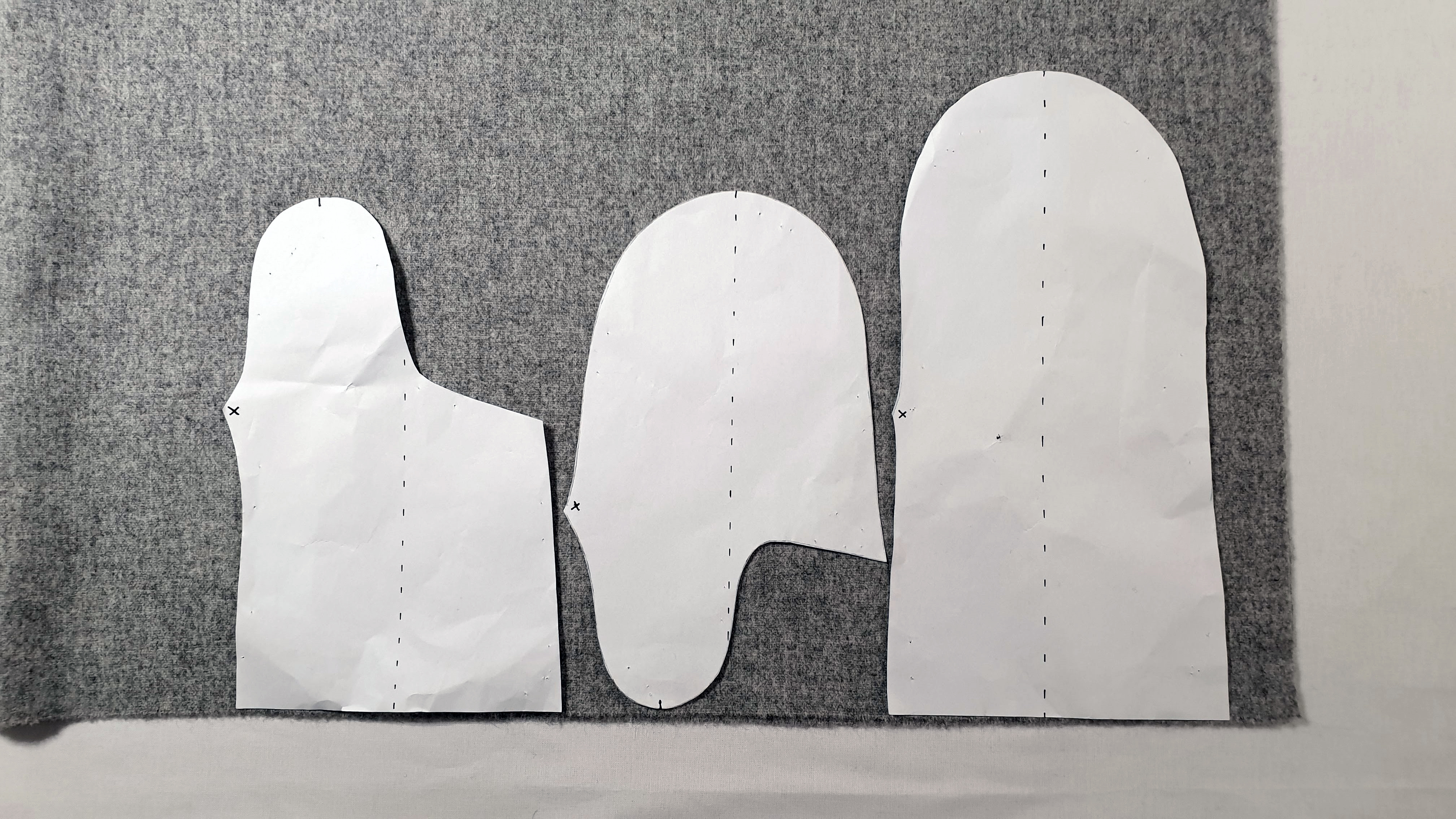 Fotografi av tre mønsterdeler i papir som ligger på et grått stoff. 