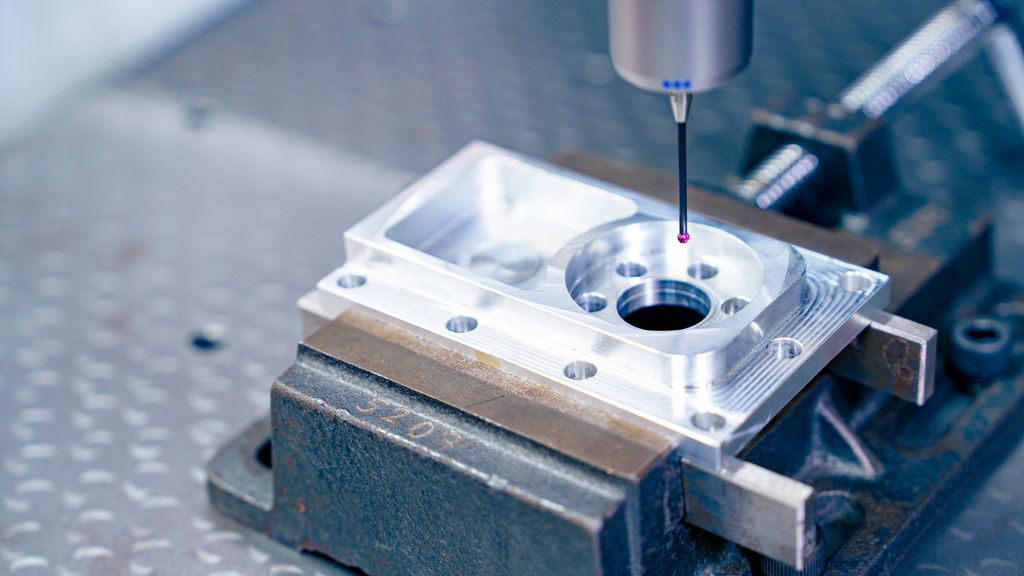 Avlang, firkanta del festa i ei maskinstikke på ei planskive. Over delen henger det en målespiss. Foto.