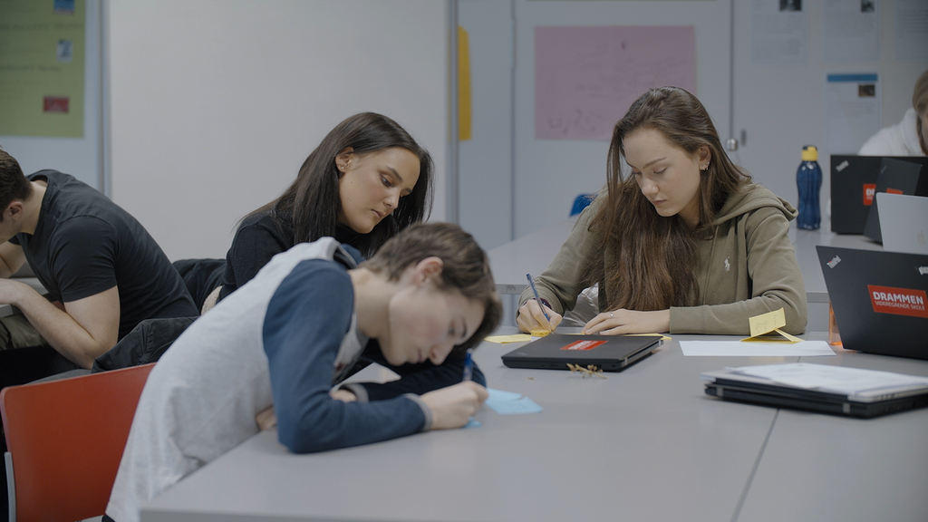 Tre elever sitter rundt et bord og noterer. De utfører kreativitetsøvelsen brainstorming. Foto.
