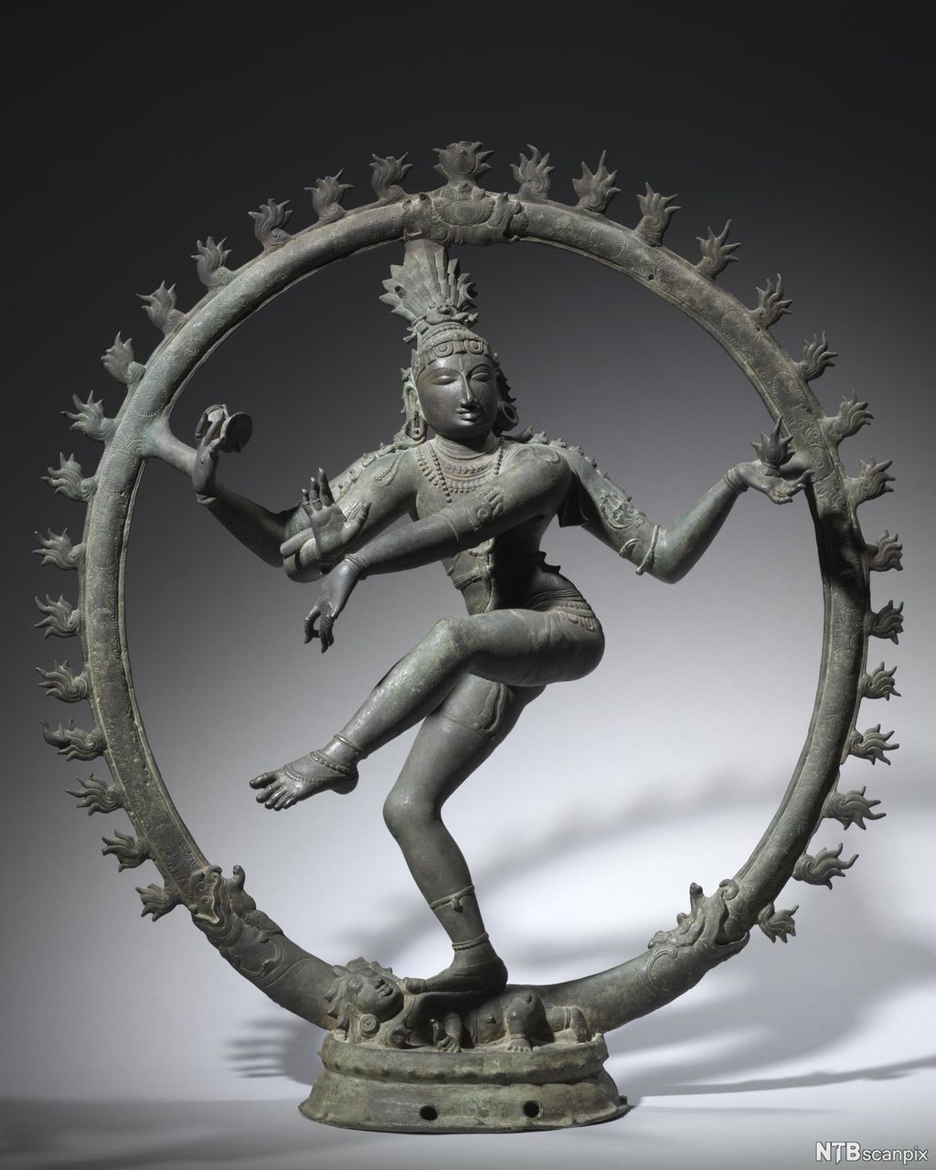 Skulptur av ein figur som dansar. Figuren har fire armar og står inni ein ring. Illustrasjon.