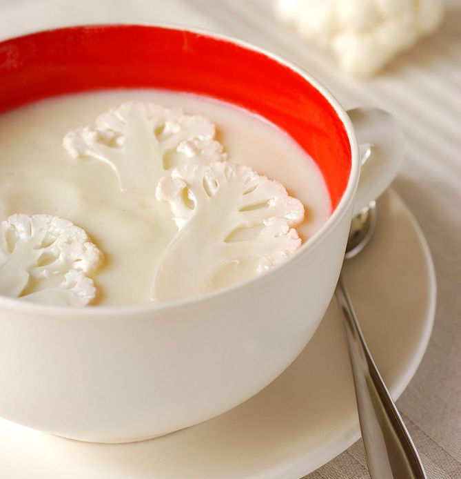 Ei skål med hvit suppe med delte blomkålbuketter i. Foto.