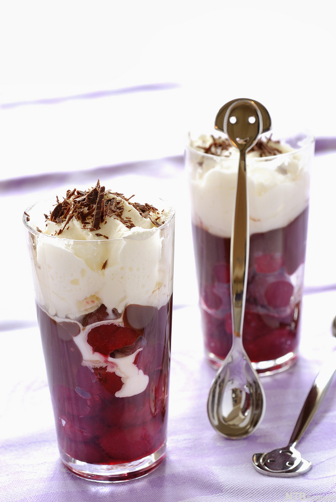Dessertglass med kirsebær i konjakk nederst og krem på toppen. Foto.