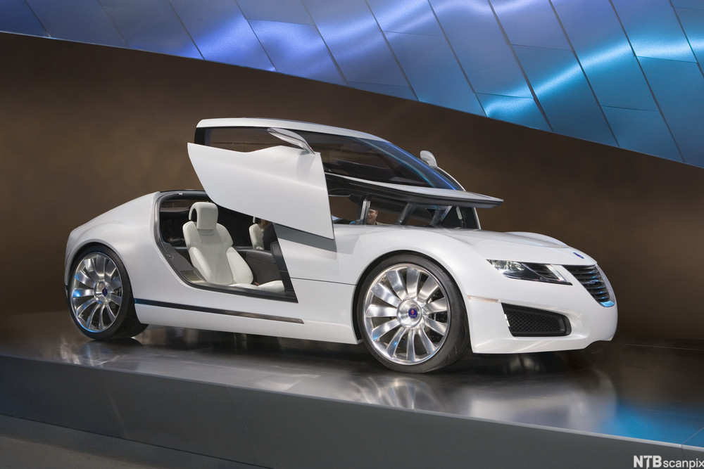 Stilig hvit bil med hevedører står på et podium. Foto.