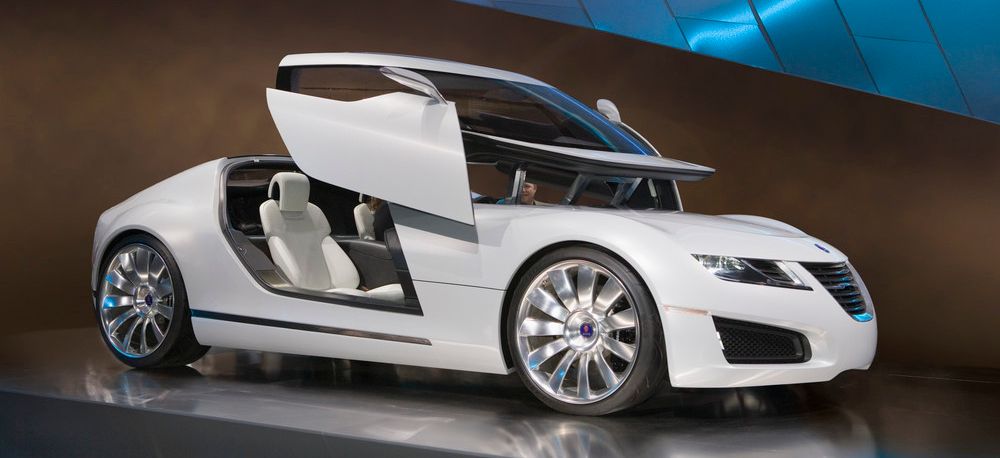 Stilig hvit bil med hevedører står på et podium. Foto.