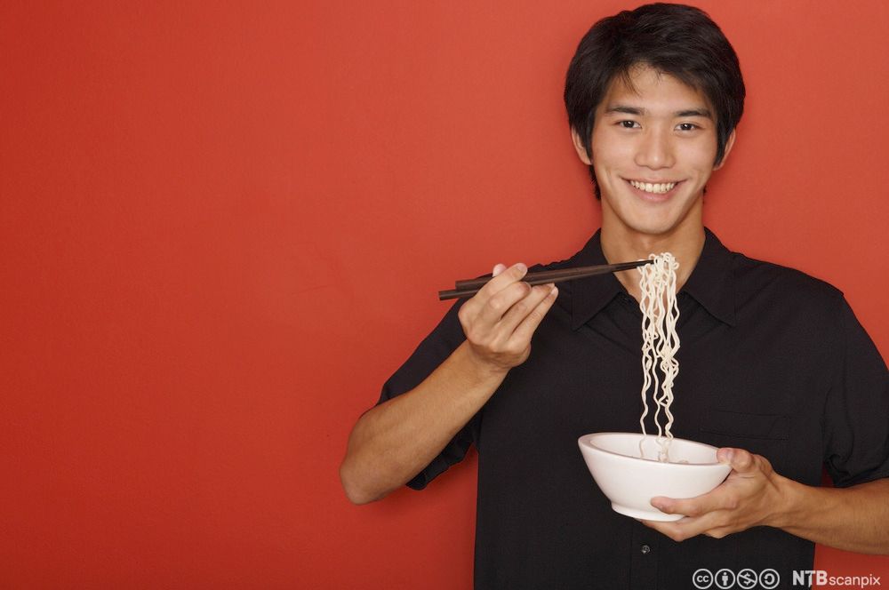 Ung mann holder en bolle med nudler. Foto.