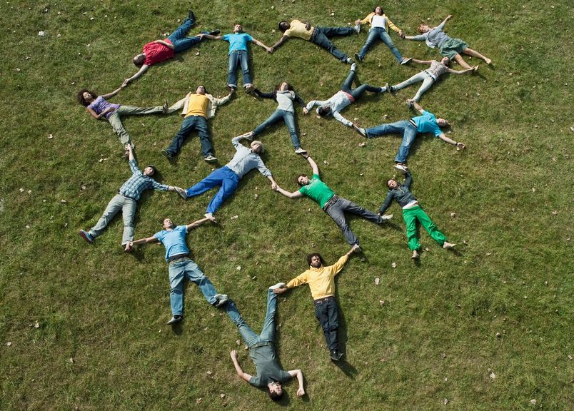 Mange personer ligger på en gressplen og holder hverandre i hender og føtter for å illustrere et nettverk. Foto. 