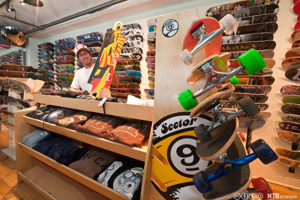 Blid mann bak disken i skateboard-butikk. Foto.