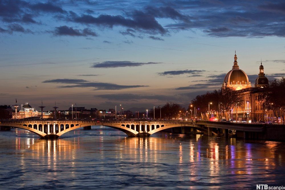 Byen Lyon om natta. Ei bru er lyst opp av lysa i byen, og elva speglar seg i lysglansen. Bygningane rundt er gamle og ærverdige. Foto.