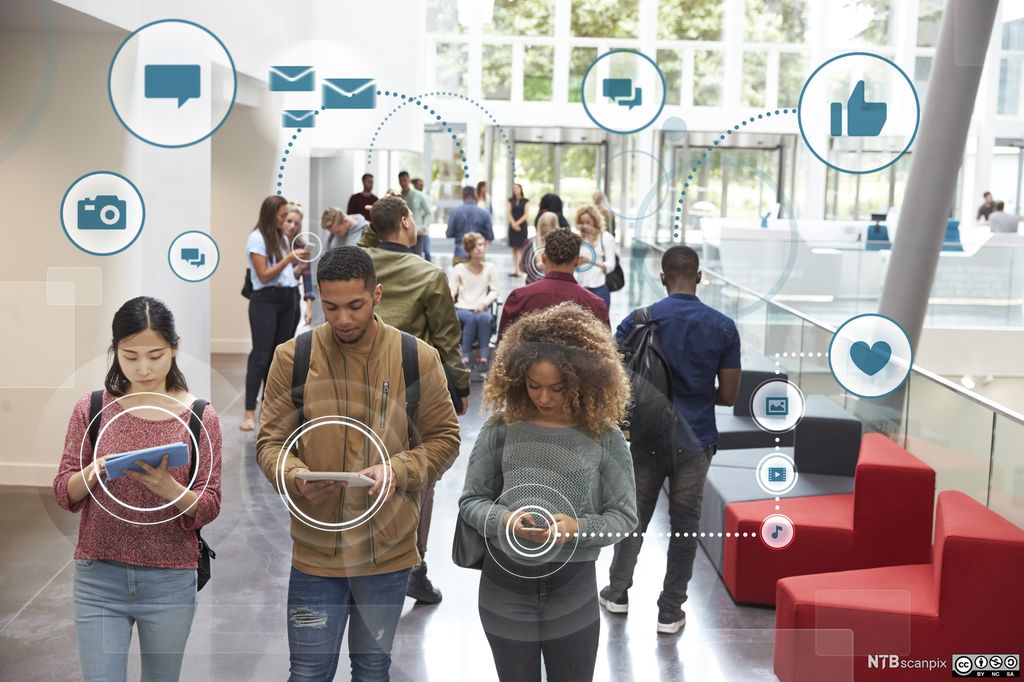 Flere ungdommer står og går i inngangspartiet til et moderne bygg. De bruker mobiltelefoner og nettbrett, og rundt dem svever ikoner som symboliserer digitale medier. Illustrasjon.