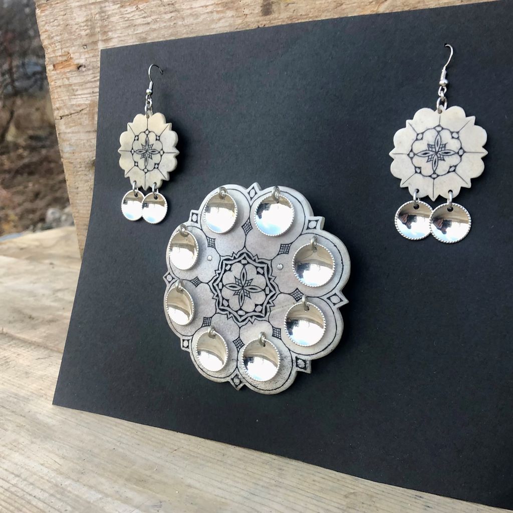 To øredobber og ei sølje av horn med mønster og sølvpynt festa på ei svart plate. Foto.