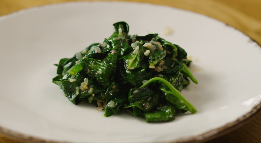 Sautert spinat anrettet på en hvit tallerken. Foto.