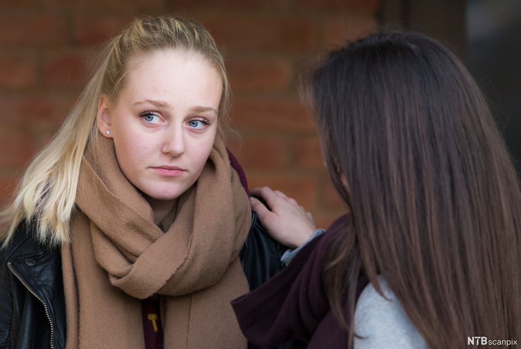 En jente får trøst av ei venninne. Jenta som trøstes, har et trist blikk og ser bort. Jenta som trøster, holder ei hånd på skulderen til venninnen. Foto.