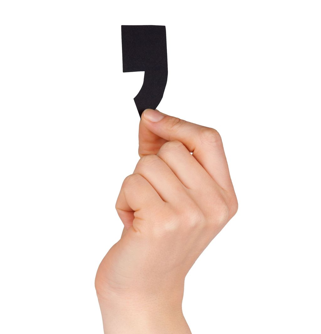 A hand holding up a black comma. Photo.