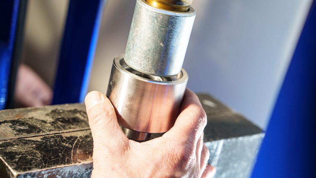 Hånd som holder to sylindriske deler. Foto.