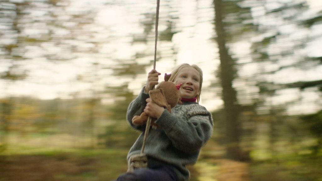 Ei jente i strikkegenser held ein bamse mens ho leiker i eit slengtau. Stillbilde frå filmen Systemsprengeren.