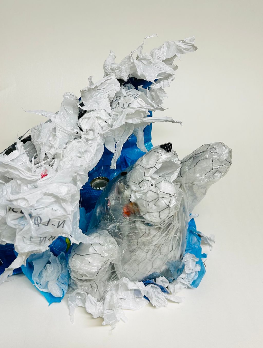 Skulptur av en isbjørn av plast og hønsenetting som kjemper under en bølge av plast. Foto.