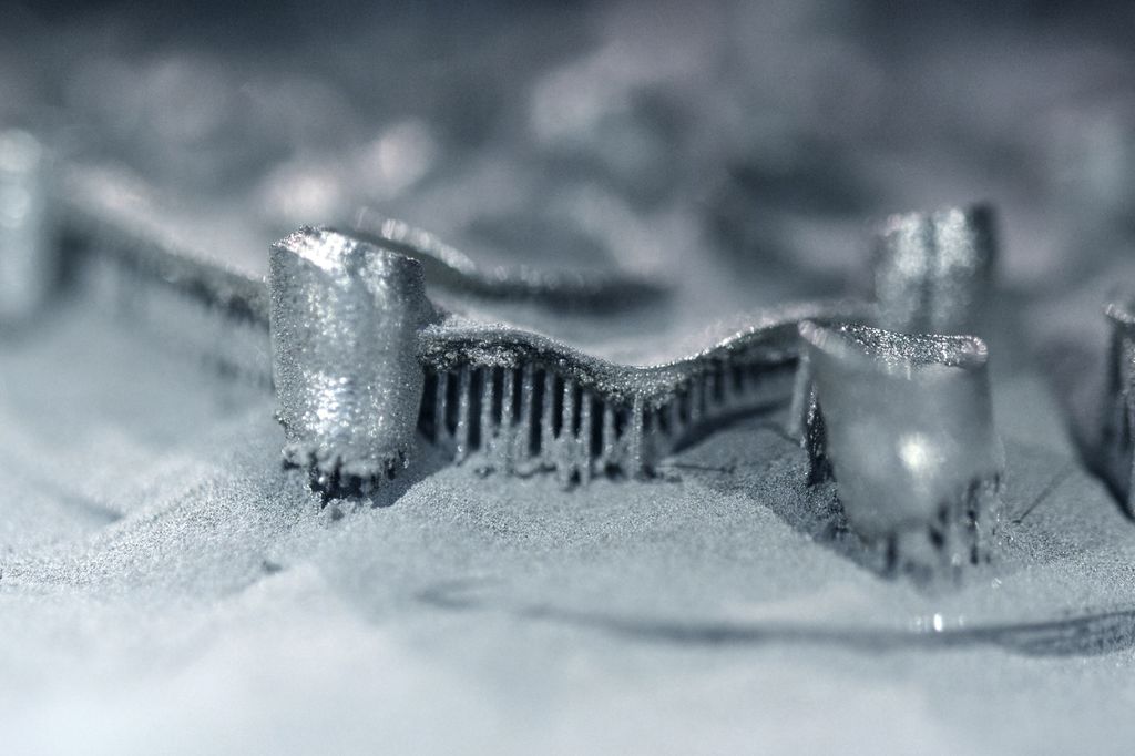 Metallisk struktur i en haug av fint, grått pulver. Foto.