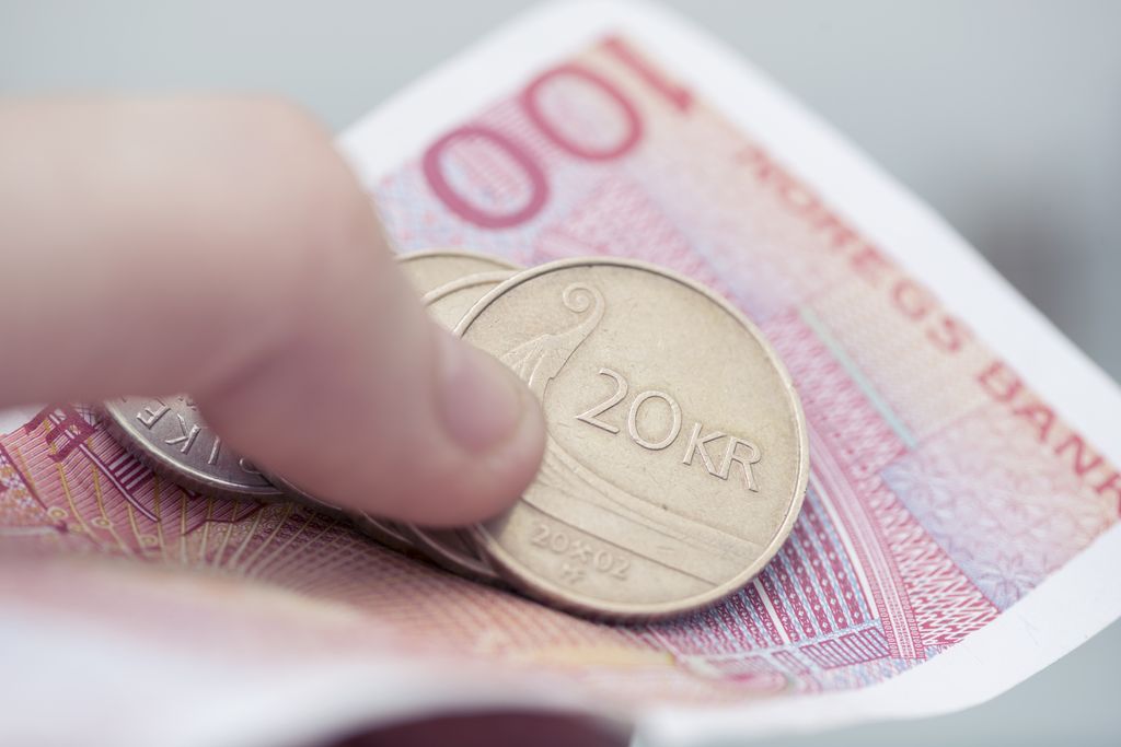 Hånd som holder i norske mynter og sedler. Foto.