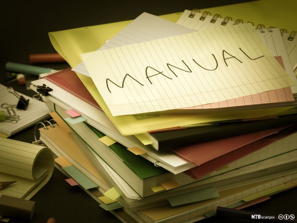 Stabel med blokker og permer med notatlapper og et ark hvor det står "manual" på toppen. Foto.