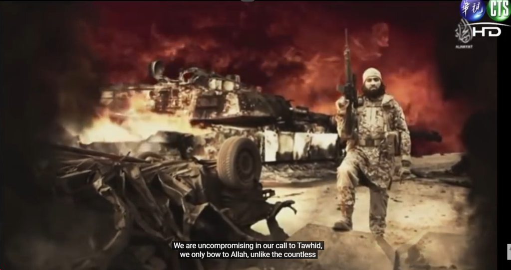 Brennende bilvrak og en soldat med maskingevær og mørkt skjegg i forgrunnen. I bakgrunnen ei stridsvogn og en ulmende brann. Filmteksting nederst som følger: "We are uncompromising in our call to Tawhid, we only bow to Allah". Skjermdump.