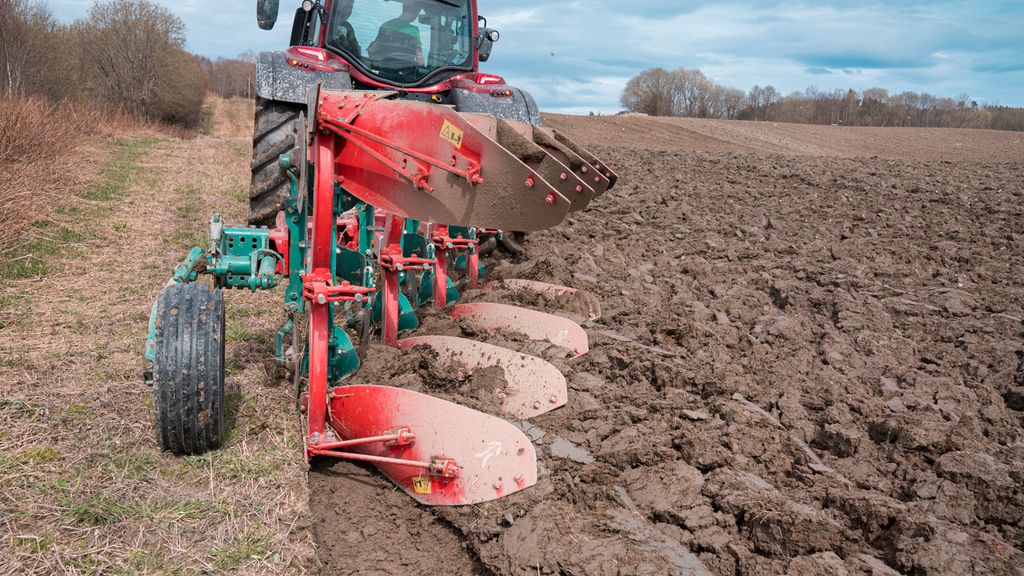 En traktor drar plogen etter seg på et stort jorde som nesten er ferdigpløyd. Foto.