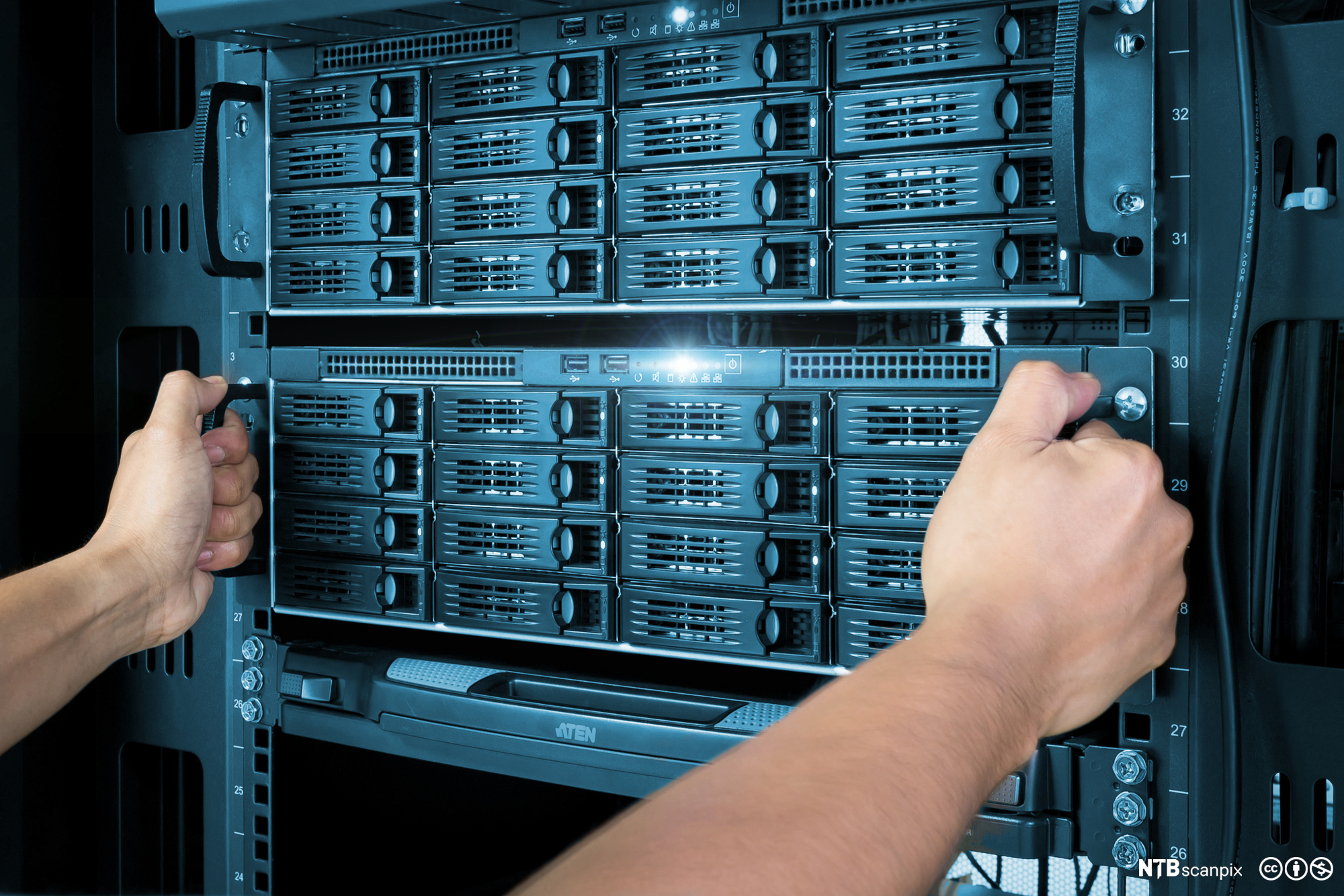 Person drar ut en lagringsserver med mange harddiskskuffer ut fra et serverskap. Foto.