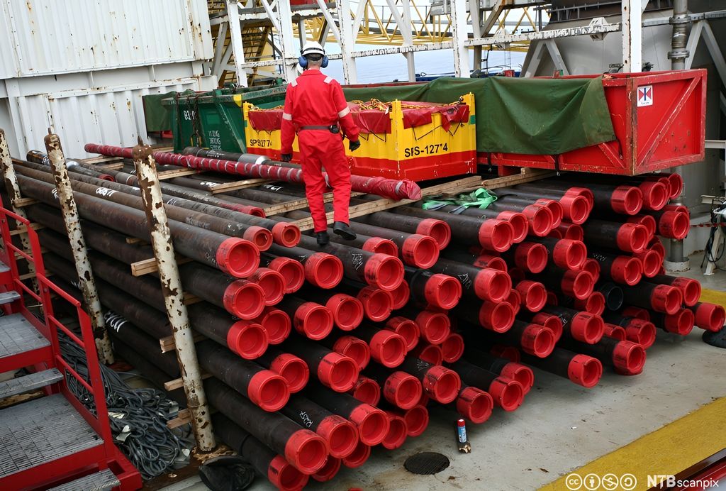 En boredekksarbeider går på toppen av en stabel med oljerør på en oljeplattform. Foto.