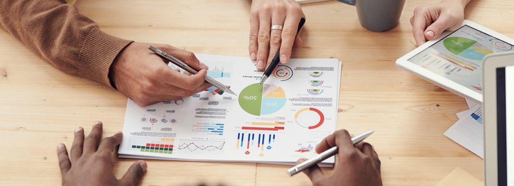 Hender fra forskjellige personer peker på grafer og diagrammer på et ark. Foto.