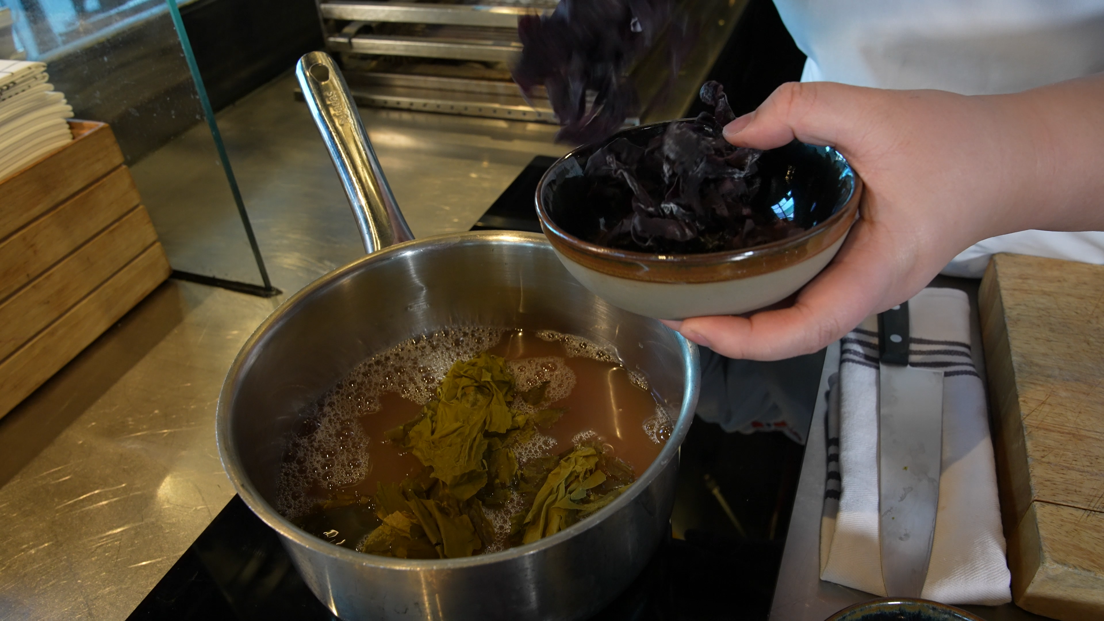 Ei gryte med fiskekraft. En kokk er i ferd med å tilsette tang og tare i gryten. Foto.