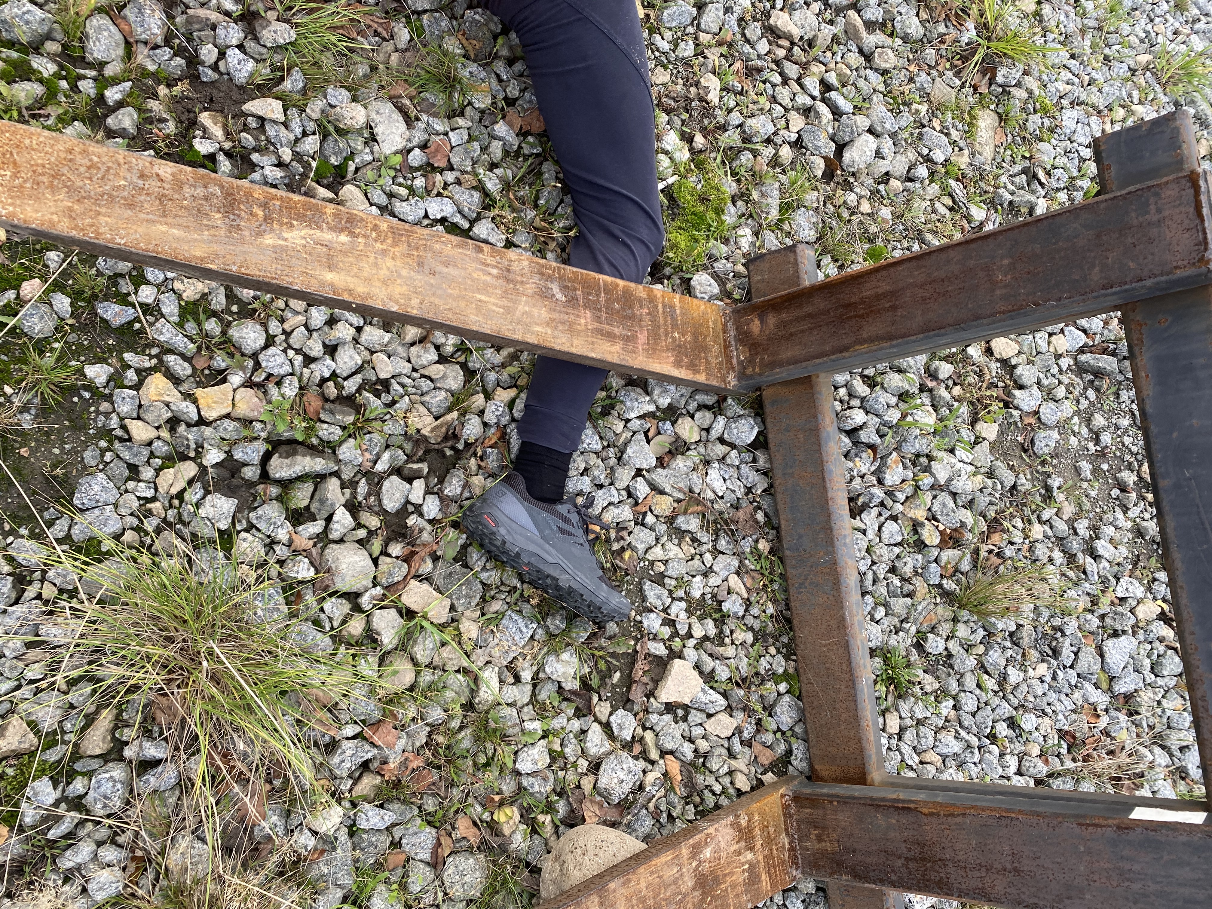 Bein til person som ligger på bakken. En tykk metallstang ligger over leggen til personen. Foto.