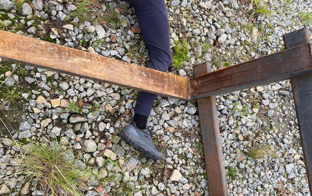 Bein til person som ligger på bakken. En tykk metallstang ligger over leggen til personen. Foto.